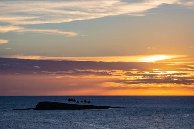 Silhouette of a tiny palm-fringed islet in the Abrolhos archipelago set against a vivid orange and pink sunset sky