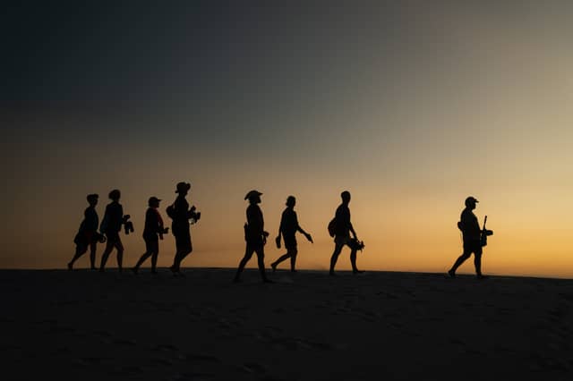 Silhouettes of a guided group hiking in Brazil across open sand dunes beneath a vivid orange and grey sunset sky
