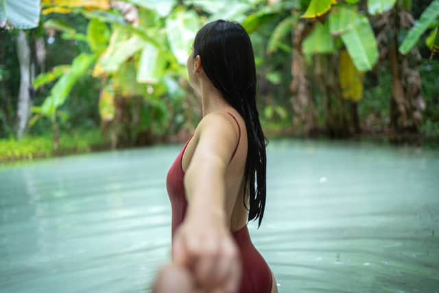 A woman in a red swimsuit wading through a calm, milky-green natural pool surrounded by lush tropical vegetation on a Jalapão tour