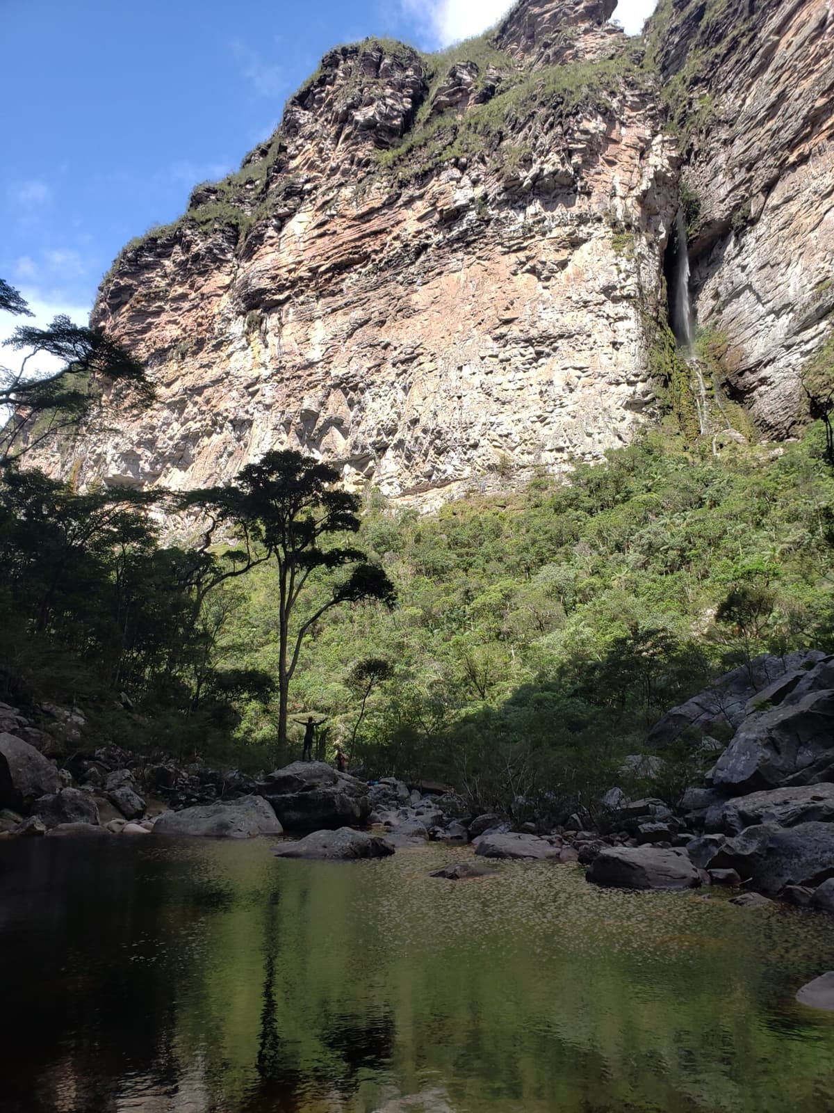 Hiker standing beneath the towering Cachoeirão waterfall in Chapada Diamantina