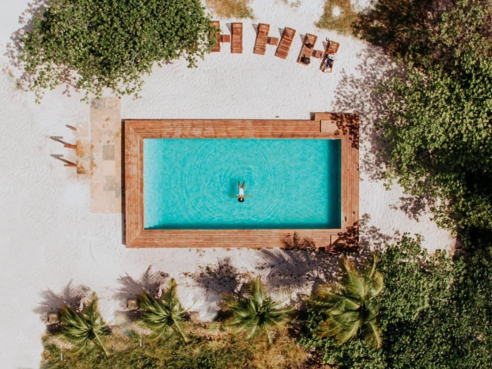 Vertical aerial shot of a rectangular turquoise swimming pool with a smooth wooden deck and loungers at the luxurious La Ferme De Georges.