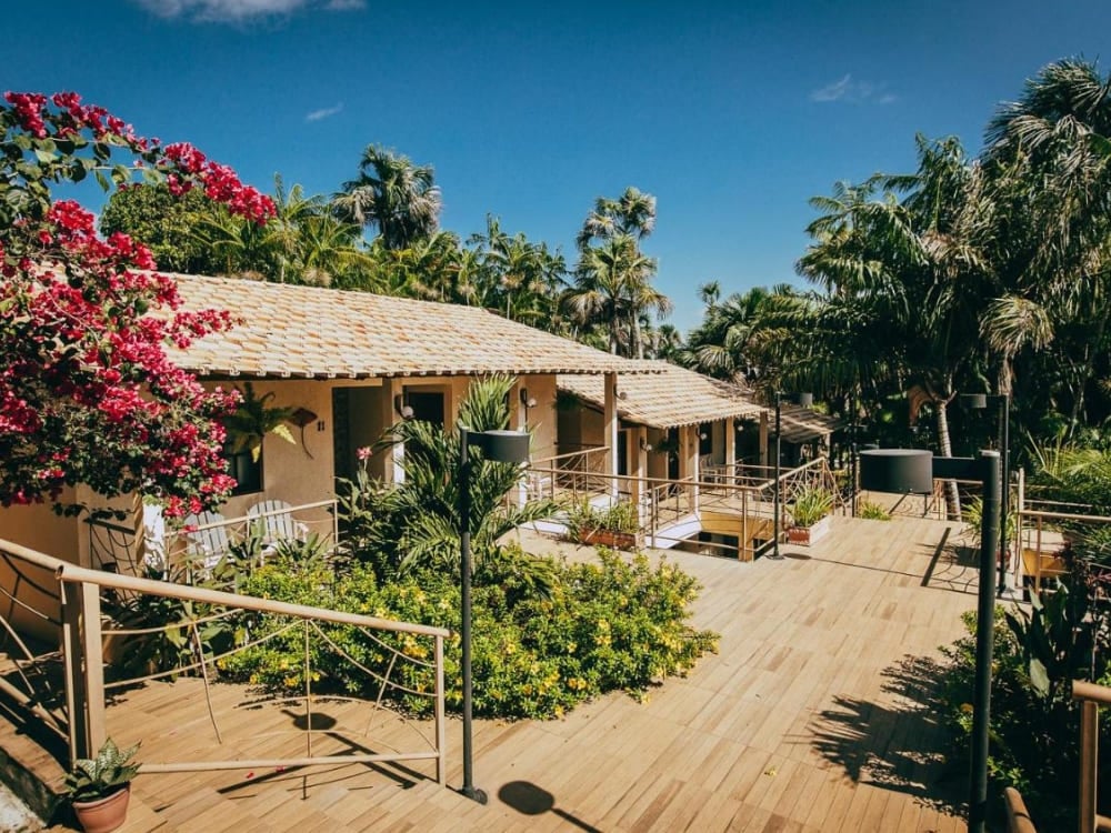 Sunny outdoor area of a rustic inn with a flowery garden, wooden ramps, and stairs connecting the room balconies.