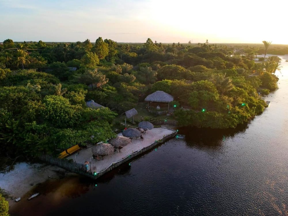 Aerial view of the camp-style Ciamat Camp, highlighting thatched kiosks and a deck by the water surrounded by vegetation.
