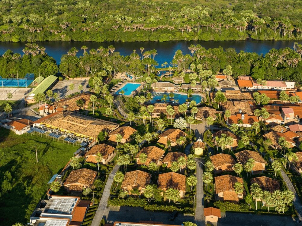 Aerial view of the large swimming pools and clay-roofed chalet infrastructure at Porto Preguiças Resort, bordering the river.