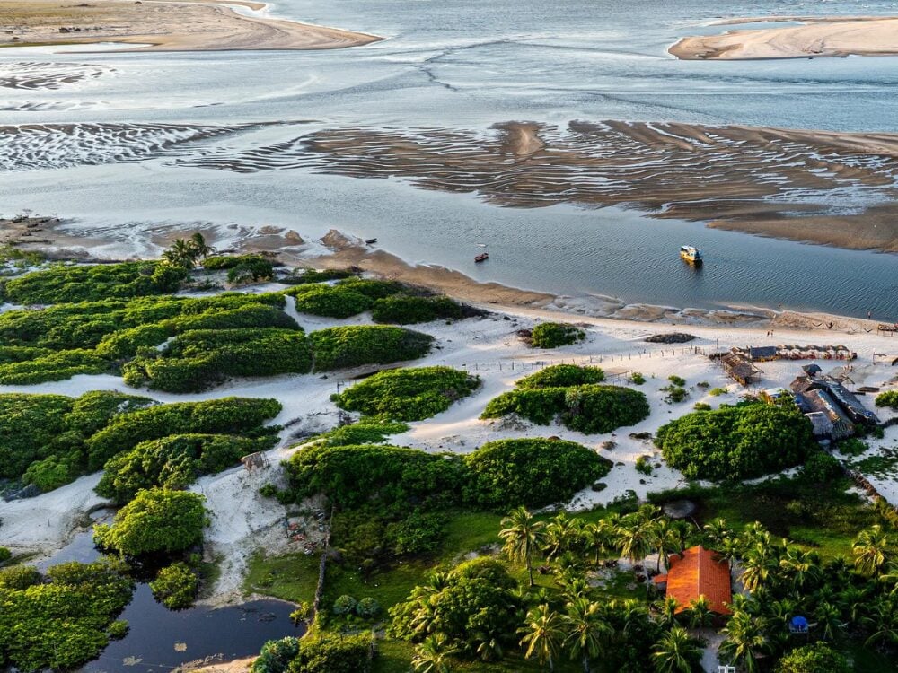 Lush aerial landscape of Atins, highlighting the green vegetation, sandbanks, and the meeting of the Preguiças River waters with the ocean.
