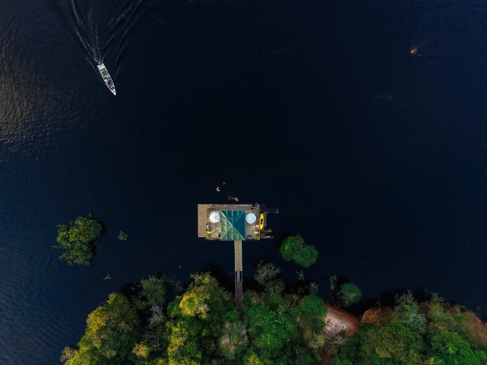 Aerial drone shot of an eco-lodge built on stilts surrounded by the dark waters of the Amazon river and lush jungle.