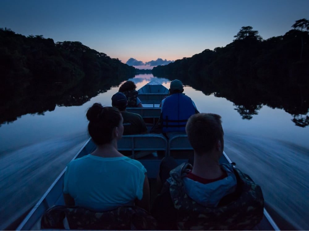Tourists riding a motorized canoe exploring the calm waters of the Amazon Rainforest river at dusk