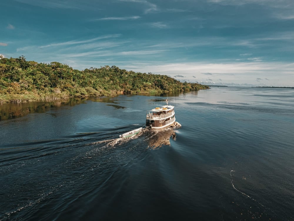 A river cruise boat navigating the calm waters of the Amazon River surrounded by lush green jungle.