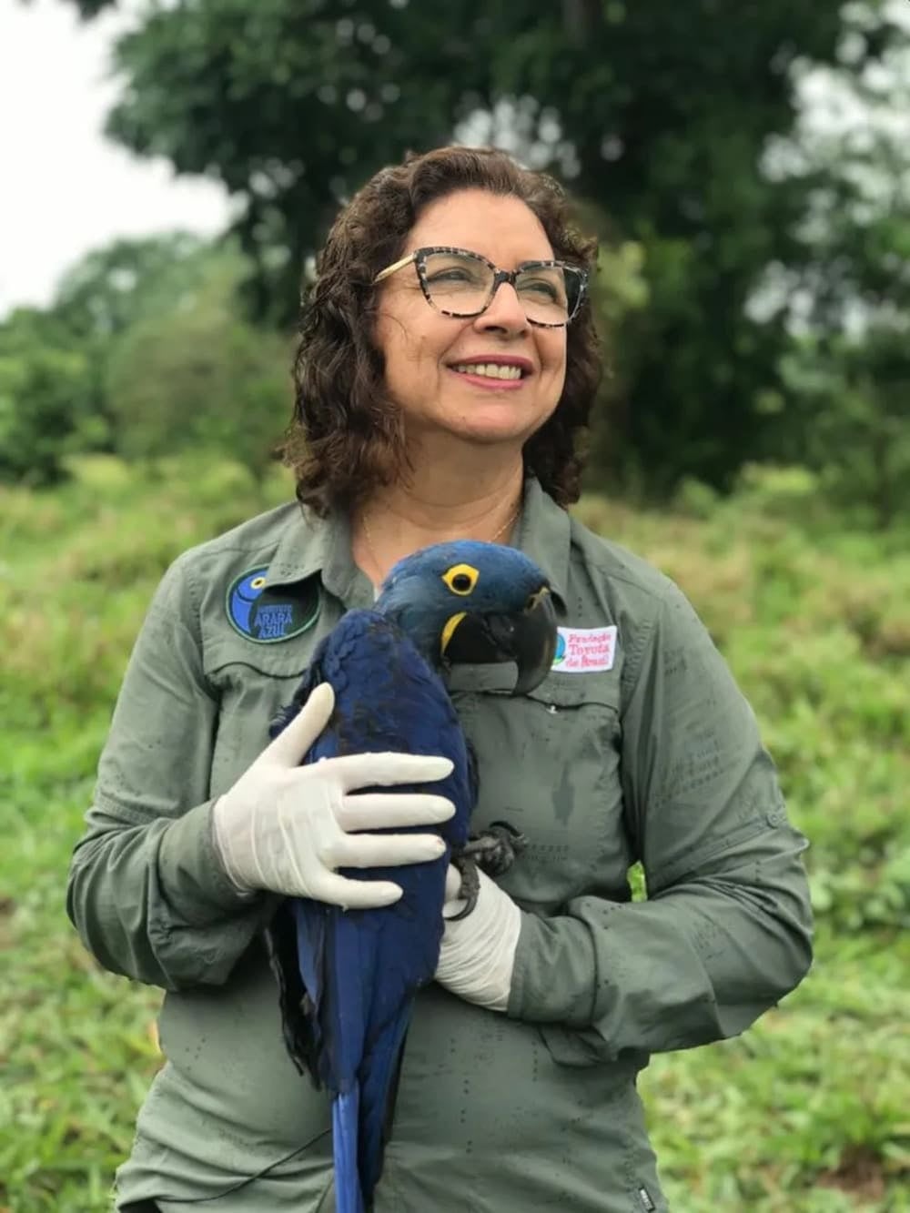 Biologist Neiva Guedes smiles while gently holding a blue hyacinth macaw outdoors.