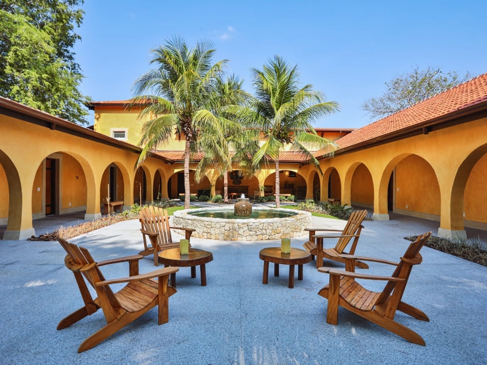 An elegant courtyard of one of the many Pantanal lodges, featuring yellow arches and wooden chairs around a fountain.