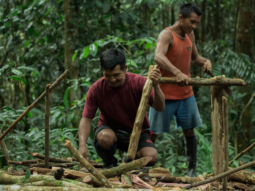 Two local guides building a wooden structure during a jungle survival tour in the Amazon.