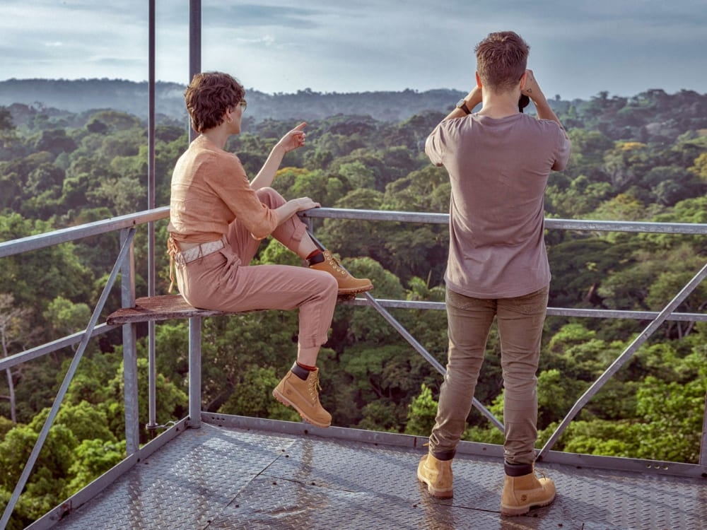 Travelers using binoculars on an observation tower high above the canopy to safely spot birds and wildlife in the Amazon Rainforest.