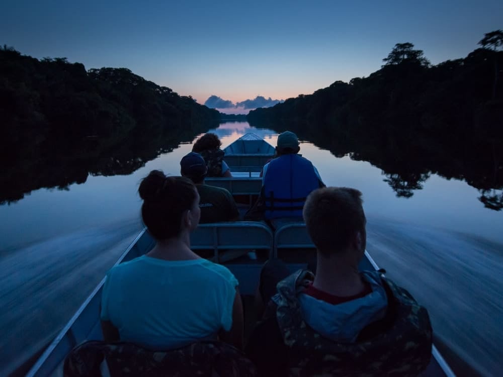 Tourists enjoying a peaceful boat ride on an Amazon river at twilight, observing nature with a local guide to ensure a safe experience.