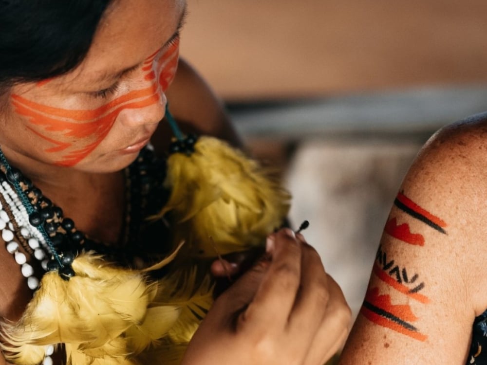 Indigenous woman applying traditional red and black face paint, representing the rich culture of local communities in the Amazon supported by ecotourism.