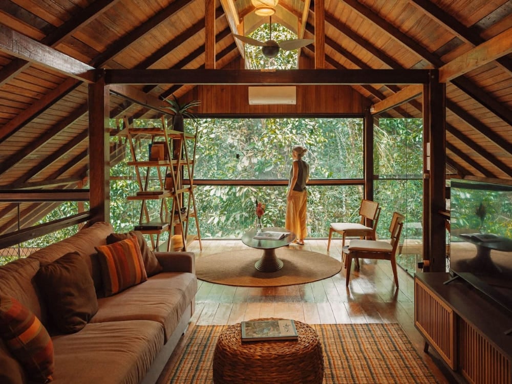 Best Amazon Jungle Cozy lounge area inside an Amazon jungle lodge with large glass windows offering immersive views of the surrounding dense forest.