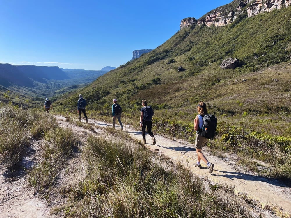 Hikers wearing comfortable shoes and carrying backpacks on a sunny dirt trail in Chapada Diamantina.