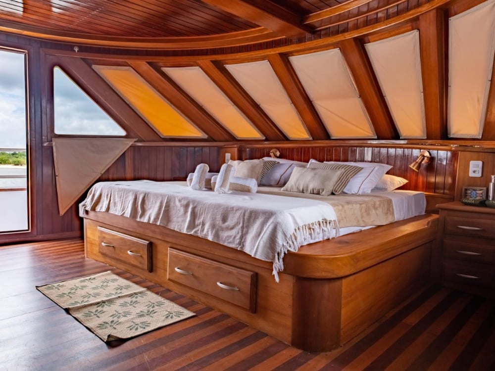 Large double bed with white sheets in a spacious cabin with a wooden ceiling on the cruise.