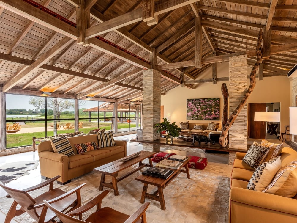 Luxurious living room with sofas, rustic wooden ceiling, and glass walls overlooking the field.