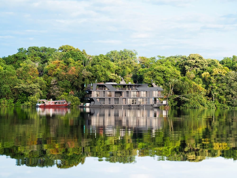 Large and luxurious river cruise ship reflected in the calm waters of an Amazon river.