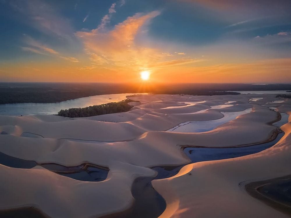 Aerial view of the dunes of Brazil with winding water channels reflecting the golden light of a vibrant sunset.