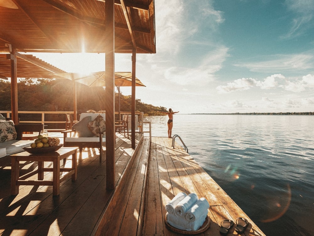 Person with open arms on the floating wooden deck of an Amazon ecolodge at sunset.