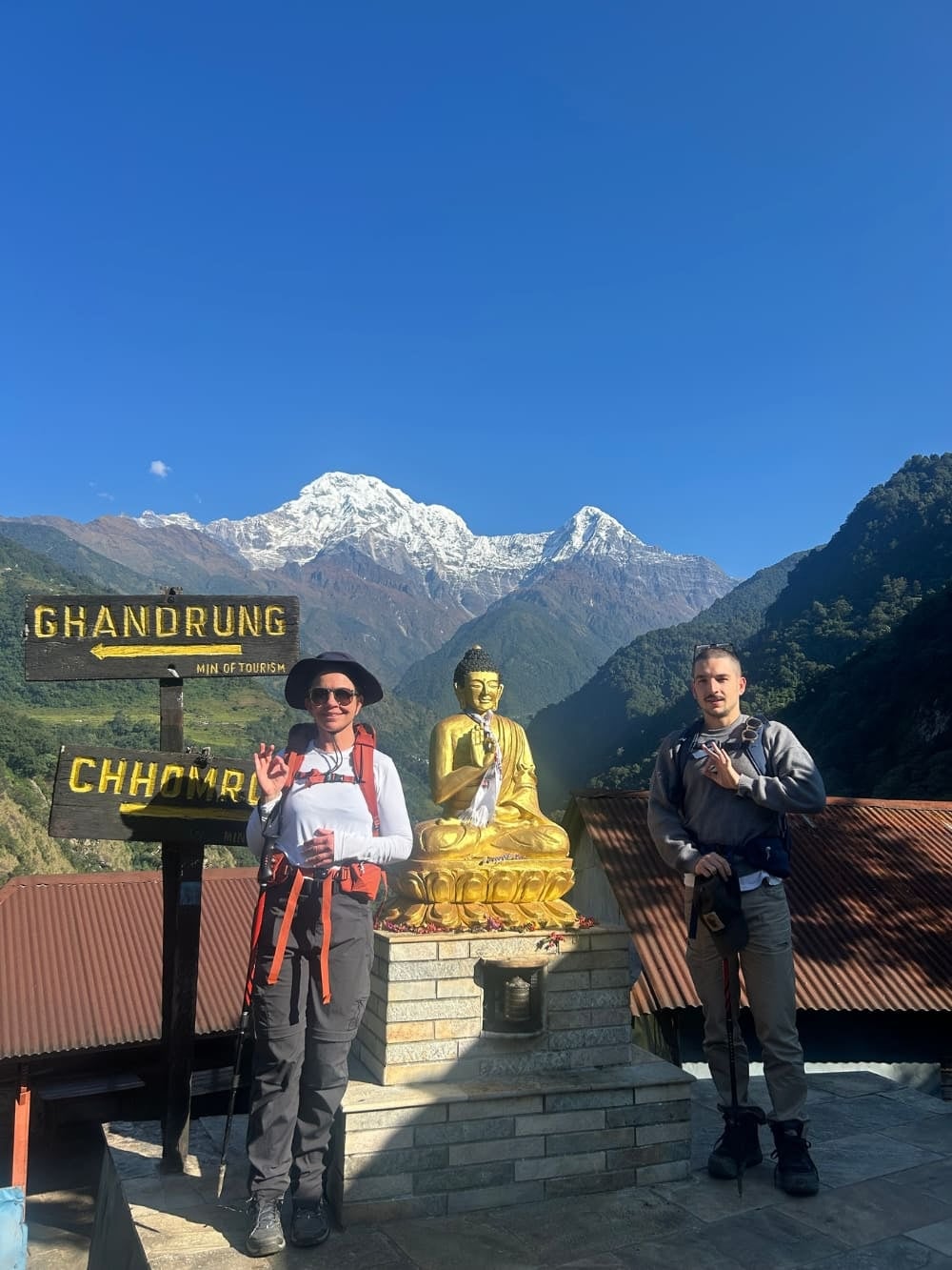 Mila and Lorenzo beside a Buddha statue and trail signs during their sustainable trek in Nepal.