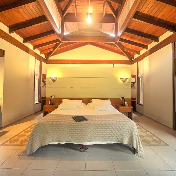 A bright suite bedroom with a vaulted, exposed wooden-beam ceiling and a large bed at an Amazon rainforest lodge.