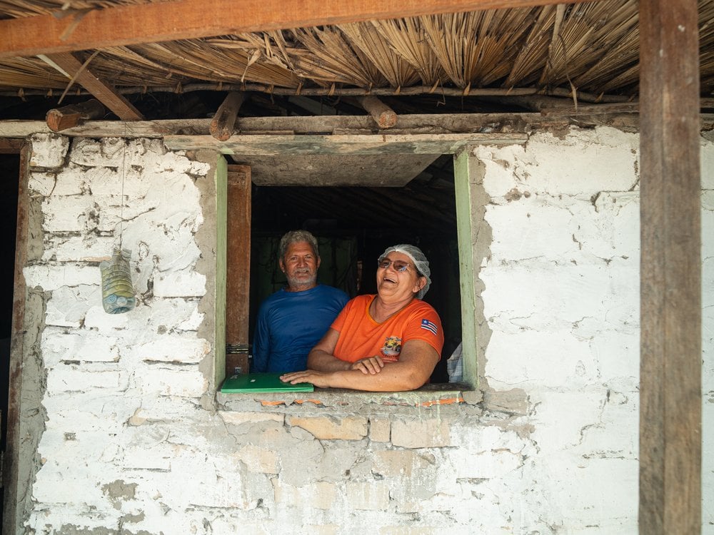 Dona Dete and Seu Moacir smiling at the window of their home in the Baixa Grande oasis