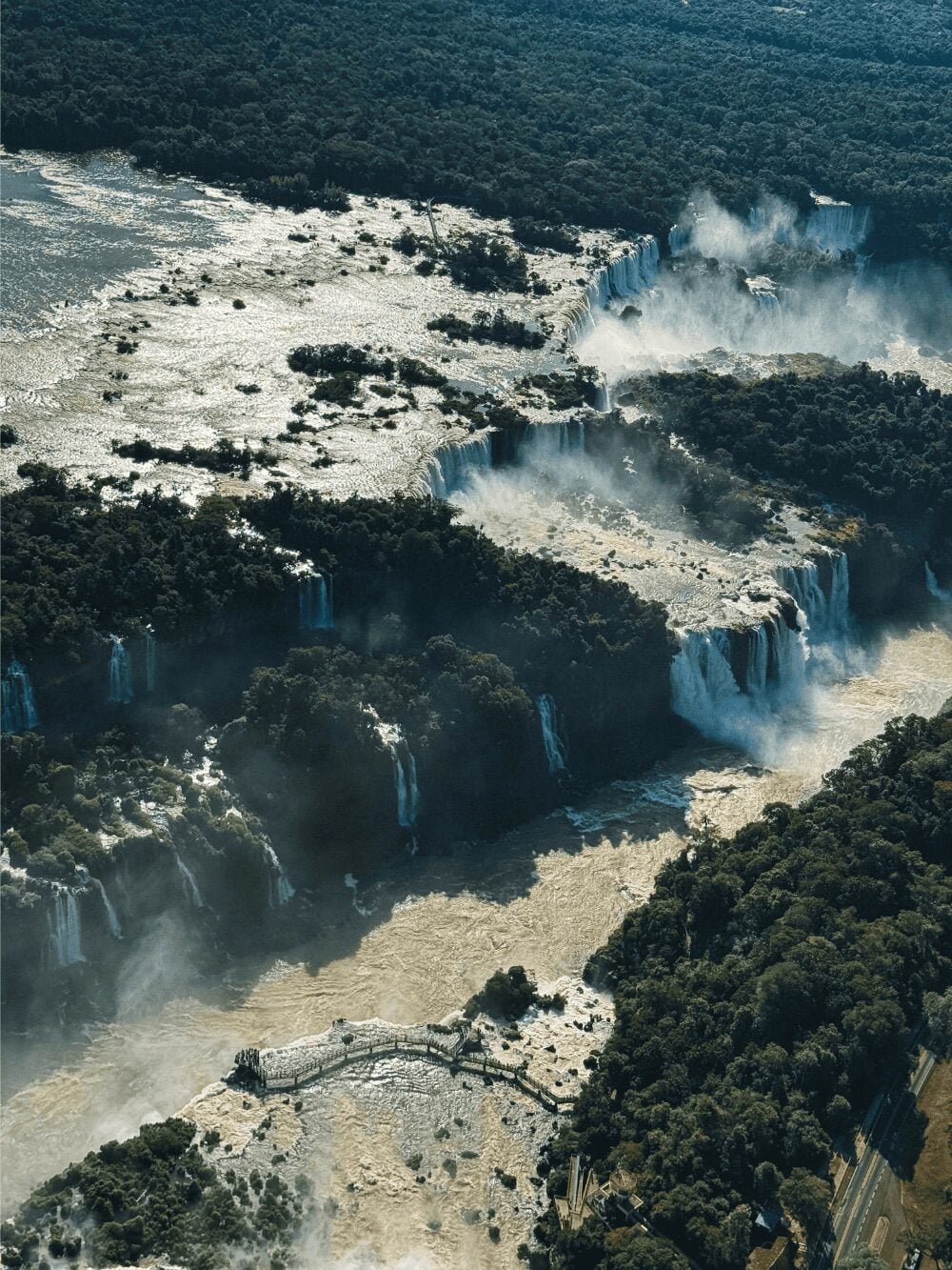 Aerial view of Iguazu Falls, with dozens of waterfalls dropping into the gorge and a walkway over the river
