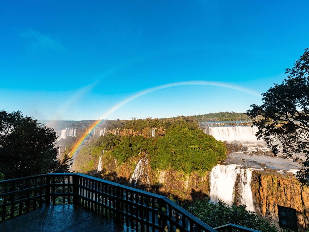 Rainbow over Iguazu Falls seen from a viewpoint railing on a clear day