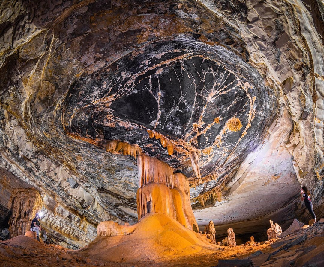 The interior of a large, illuminated cave showing an impressive cluster of ancient limestone stalactites and stalagmites. The interior of a large, illuminated cave showing an impressive cluster of ancient limestone stalactites and stalagmites.