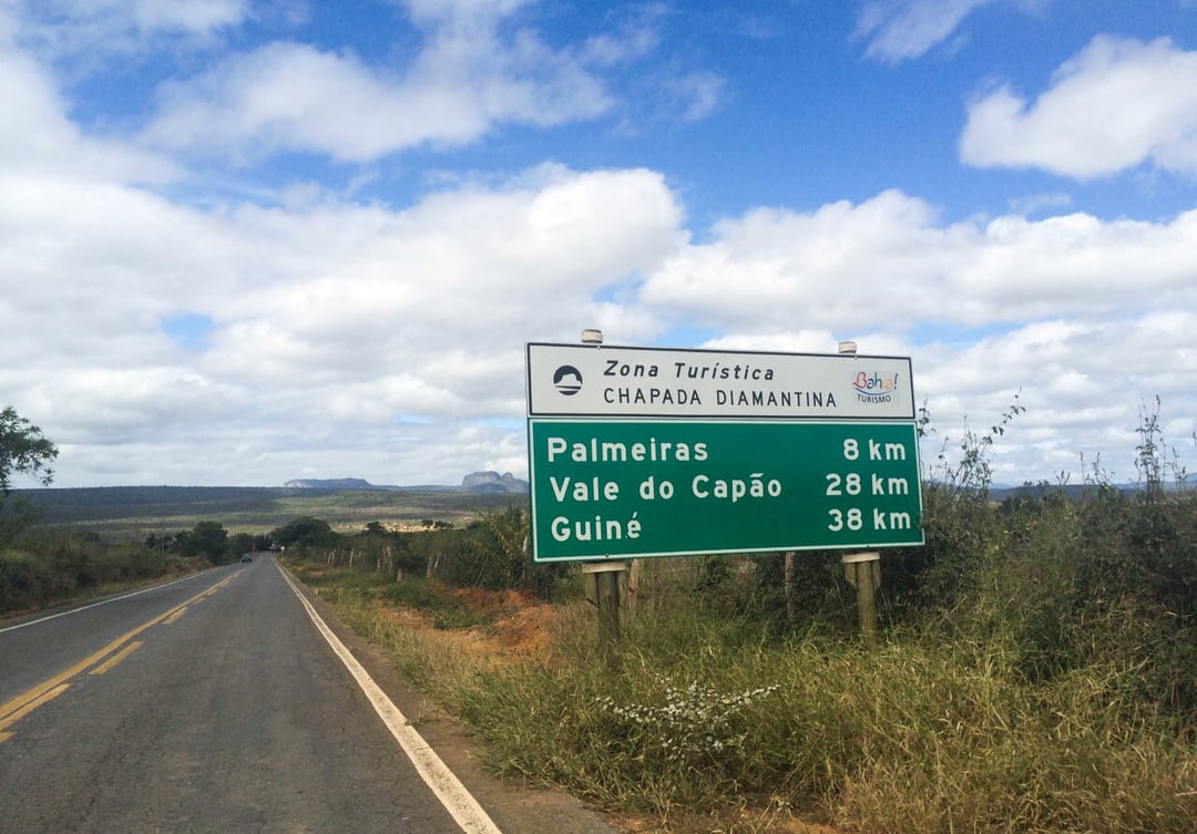 A green highway sign for the Chapada Diamantina Tourist Zone indicating distances to Palmeiras, Vale do Capão, and Guiné. A green highway sign for the Chapada Diamantina Tourist Zone indicating distances to Palmeiras, Vale do Capão, and Guiné.