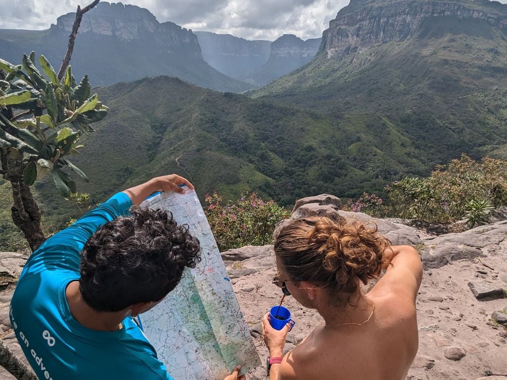 A local guide in a blue shirt and a hiker examining a trail map together while resting at a scenic valley viewpoint. A local guide in a blue shirt and a hiker examining a trail map together while resting at a scenic valley viewpoint.