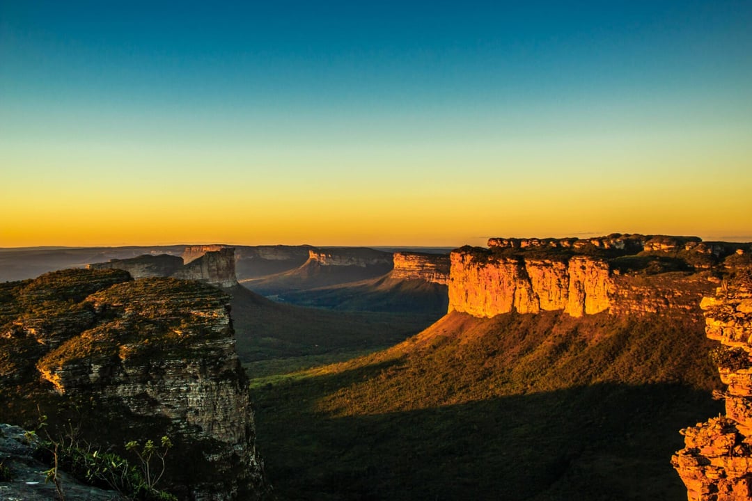 Panoramic view of Chapada Diamantina's flat-topped mountains and deep green valleys illuminated by the golden light of a sunset. Panoramic view of Chapada Diamantina's flat-topped mountains and deep green valleys illuminated by the golden light of a sunset.