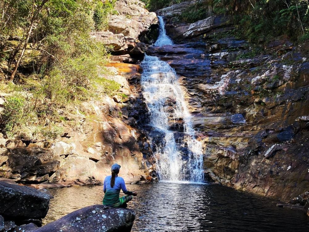 A woman sitting peacefully on a rock by the natural pool at the base of the 30-meter-high Funis Waterfall. A woman sitting peacefully on a rock by the natural pool at the base of the 30-meter-high Funis Waterfall.