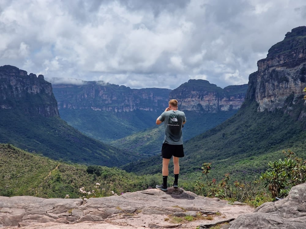 A hiker standing on a rocky outcrop taking a photograph of the sprawling green valleys and flat-topped mountains. A hiker standing on a rocky outcrop taking a photograph of the sprawling green valleys and flat-topped mountains.