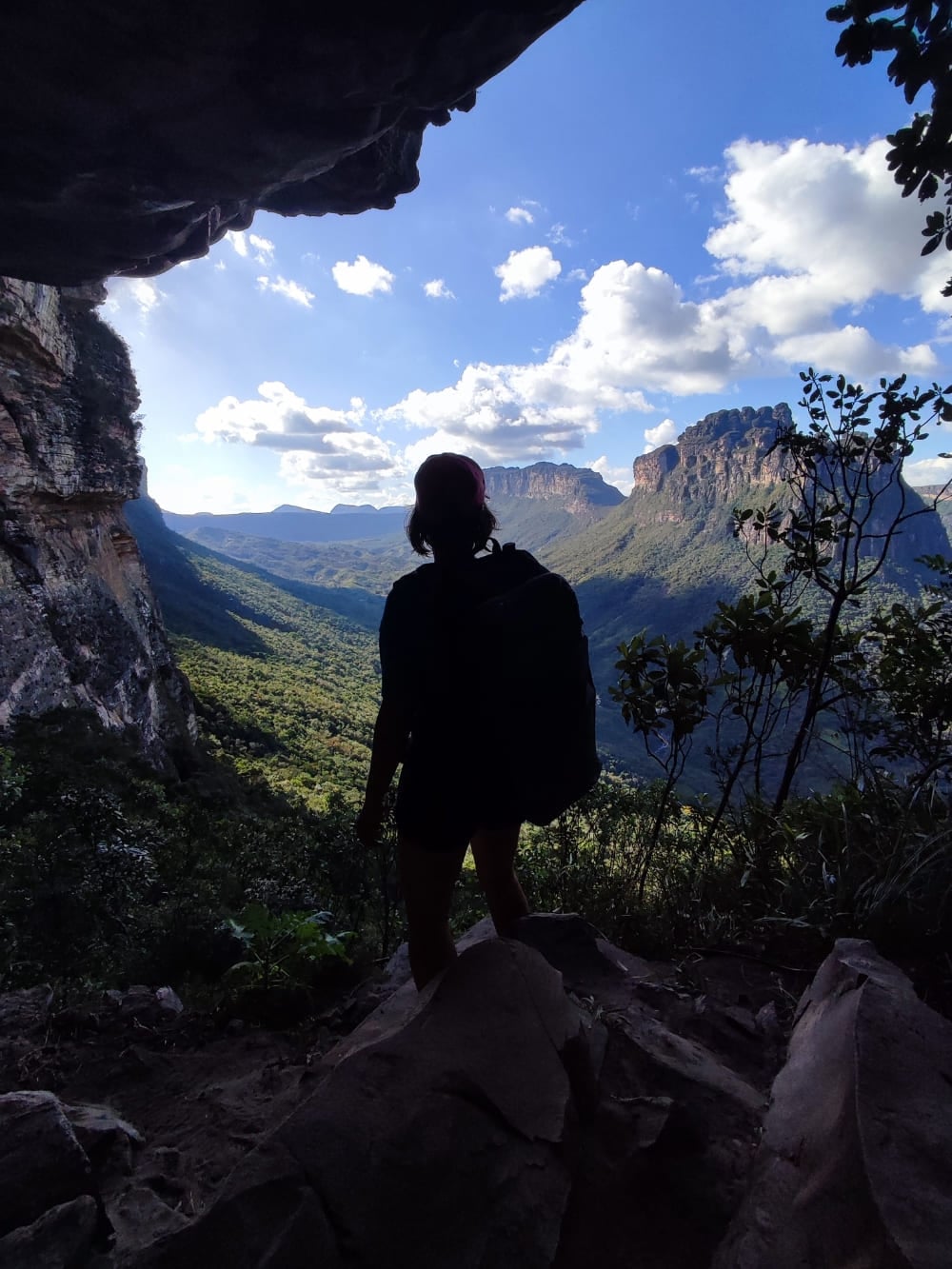 Silhouette of a hiker wearing a backpack standing at a dark cave entrance, looking out over the sunlit Pati Valley. Silhouette of a hiker wearing a backpack standing at a dark cave entrance, looking out over the sunlit Pati Valley.