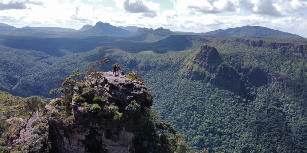 Hikers standing on a rocky peak at Morro do Castelo, overlooking a vast, forested canyon in Chapada Diamantina. Hikers standing on a rocky peak at Morro do Castelo, overlooking a vast, forested canyon in Chapada Diamantina.
