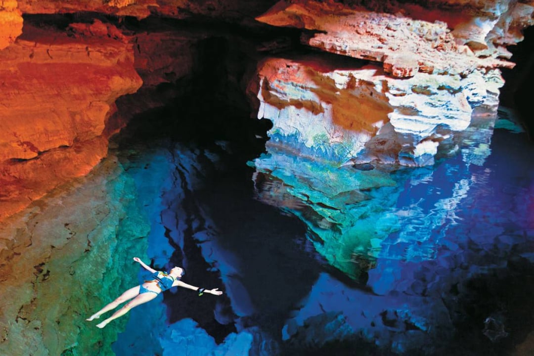 A woman floats on her back in the crystal-clear, bright blue water of an underground natural pool surrounded by rock walls. A woman floats on her back in the crystal-clear, bright blue water of an underground natural pool surrounded by rock walls.