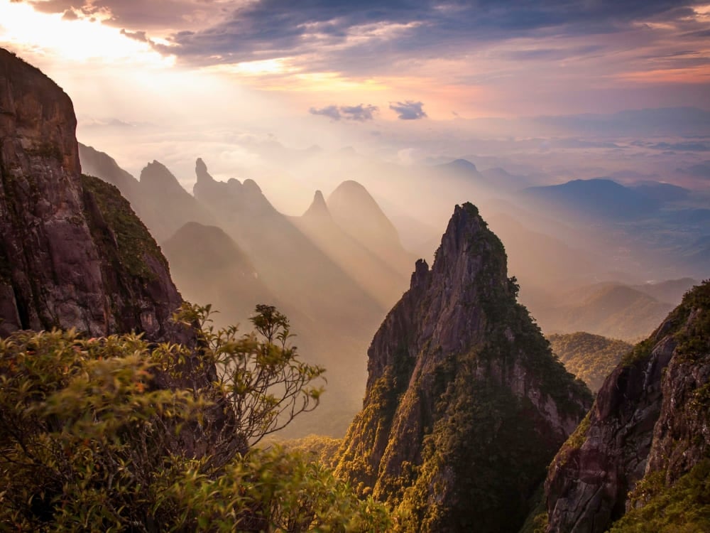 Dramatic, jagged mountain peaks emerge through thick mist at sunrise in Serra dos Órgãos National Park, highlighting the Dedo de Deus formation. Dramatic, jagged mountain peaks emerge through thick mist at sunrise in Serra dos Órgãos National Park, highlighting the Dedo de Deus formation.