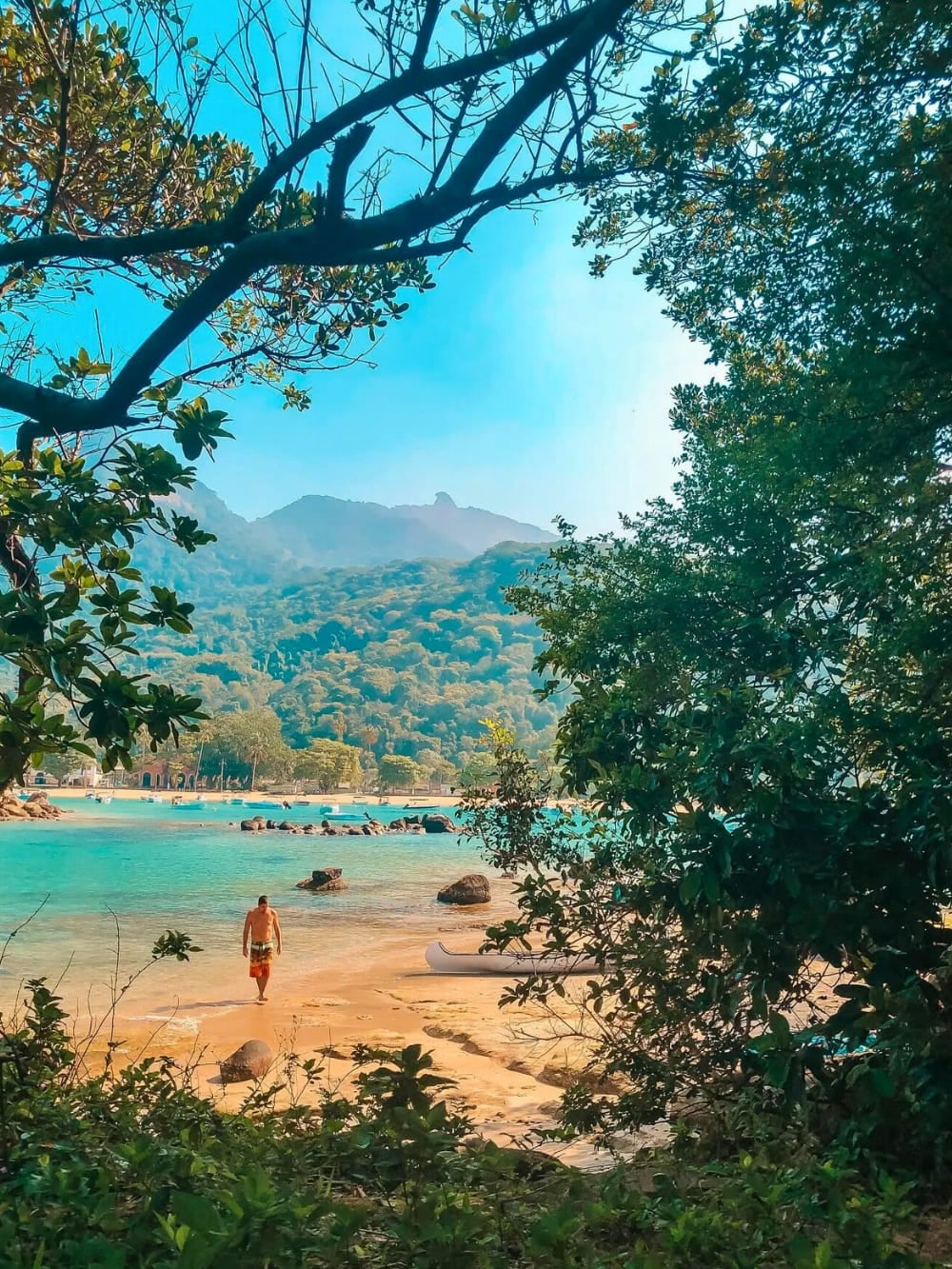 A person walks along the pristine white sand and clear blue waters of Lopes Mendes Beach in Ilha Grande, surrounded by tropical forest and mountains. A person walks along the pristine white sand and clear blue waters of Lopes Mendes Beach in Ilha Grande, surrounded by tropical forest and mountains.