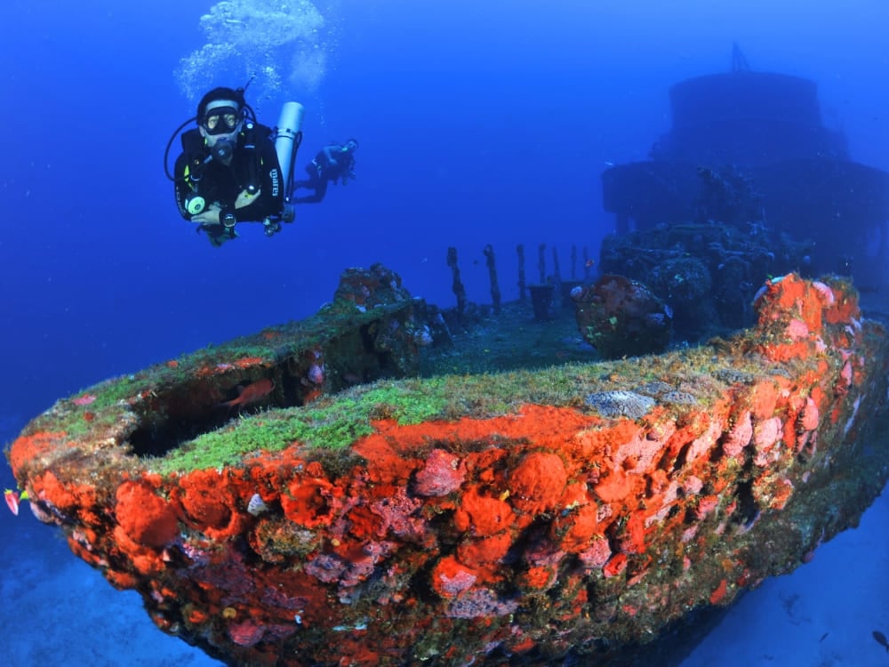 A scuba diver explores a sunken shipwreck heavily encrusted with bright red and orange sponges in the deep waters of Fernando de Noronha. A scuba diver explores a sunken shipwreck heavily encrusted with bright red and orange sponges in the deep waters of Fernando de Noronha.