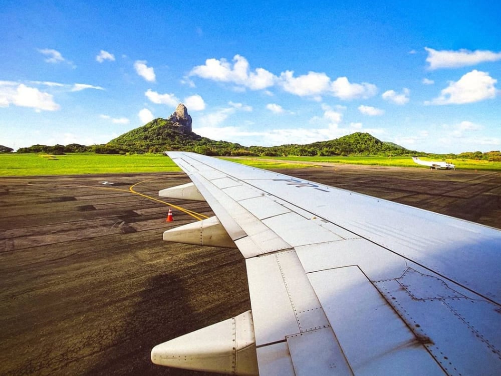 View from an airplane window showing the wing and the famous Morro do Pico peak as a flight arrives at Fernando de Noronha. View from an airplane window showing the wing and the famous Morro do Pico peak as a flight arrives at Fernando de Noronha.