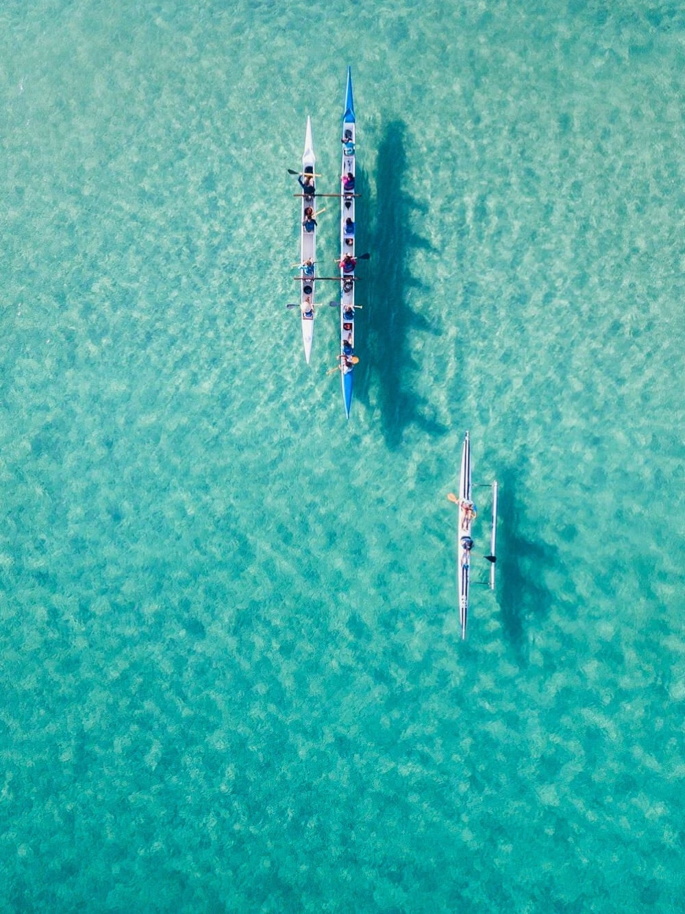 Aerial view of people paddling a traditional Hawaiian canoe through the vibrant, transparent turquoise waters of Fernando de Noronha. Aerial view of people paddling a traditional Hawaiian canoe through the vibrant, transparent turquoise waters of Fernando de Noronha.