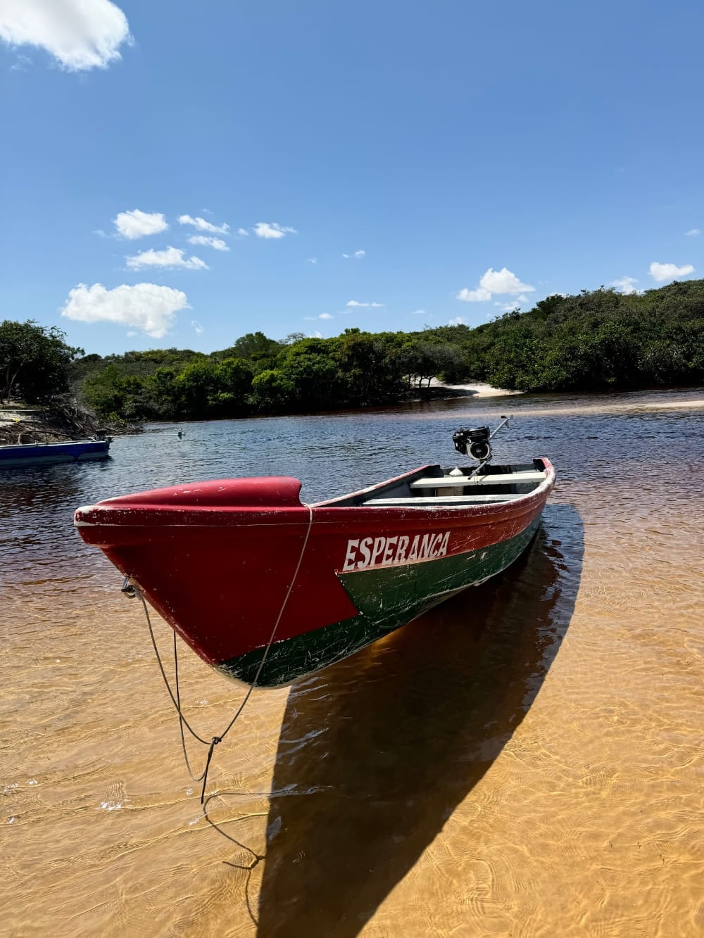 A red and green boat named Esperanca rests on the sandy shore of the dark waters of the Preguiças River. A red and green boat named Esperanca rests on the sandy shore of the dark waters of the Preguiças River.
