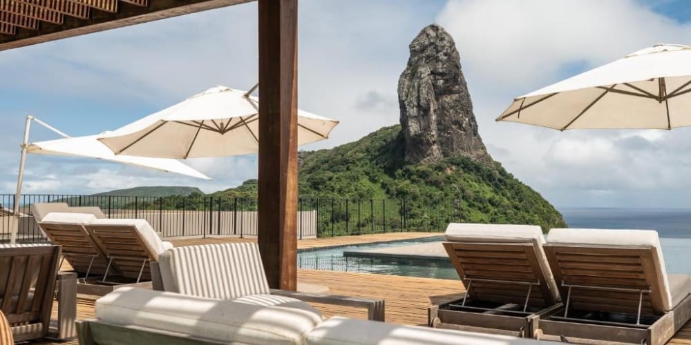 Luxury hotel deck featuring a swimming pool and comfortable lounge chairs facing the iconic Morro do Pico in Brazil. Luxury hotel deck featuring a swimming pool and comfortable lounge chairs facing the iconic Morro do Pico in Brazil.