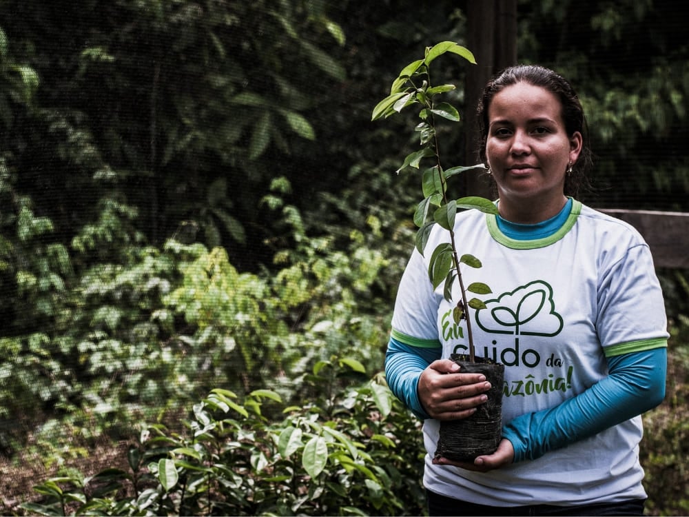 A woman holding a native tree sapling for a sustainability and reforestation project in the Amazon. A woman holding a native tree sapling for a sustainability and reforestation project in the Amazon.