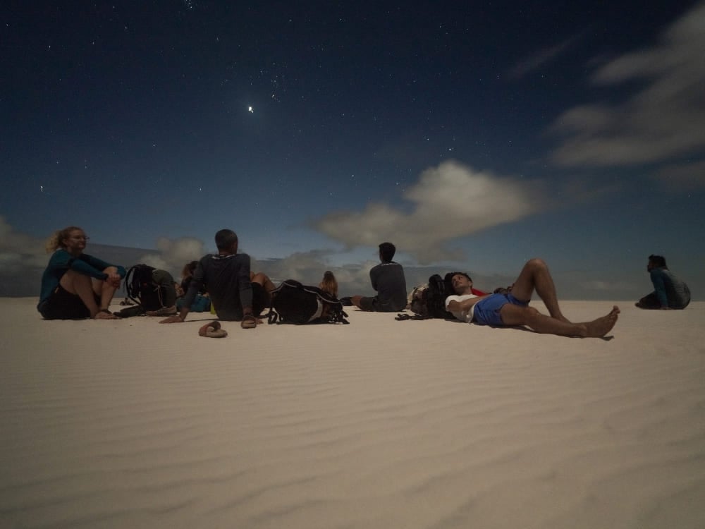 A group of travelers resting on the sand dunes under a starry night sky after a full day exploring Lençóis Maranhenses. A group of travelers resting on the sand dunes under a starry night sky after a full day exploring Lençóis Maranhenses.