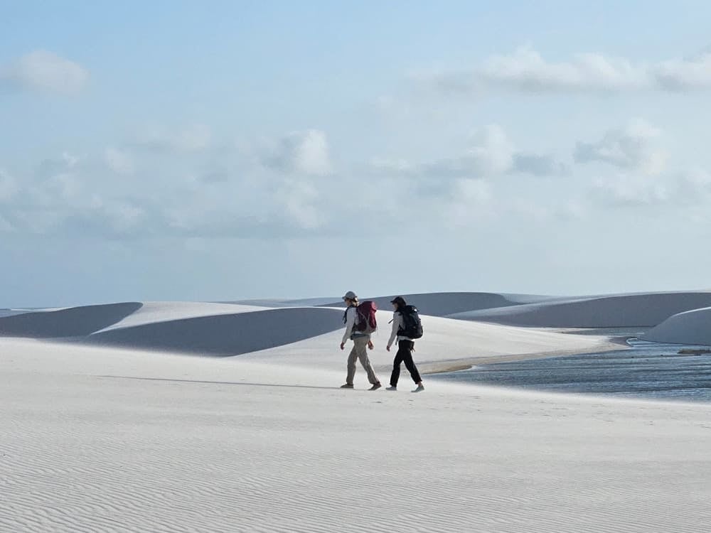 Two backpackers hike across the vast white sand dunes next to a freshwater lagoon in Lençóis Maranhenses National Park. Two backpackers hike across the vast white sand dunes next to a freshwater lagoon in Lençóis Maranhenses National Park.