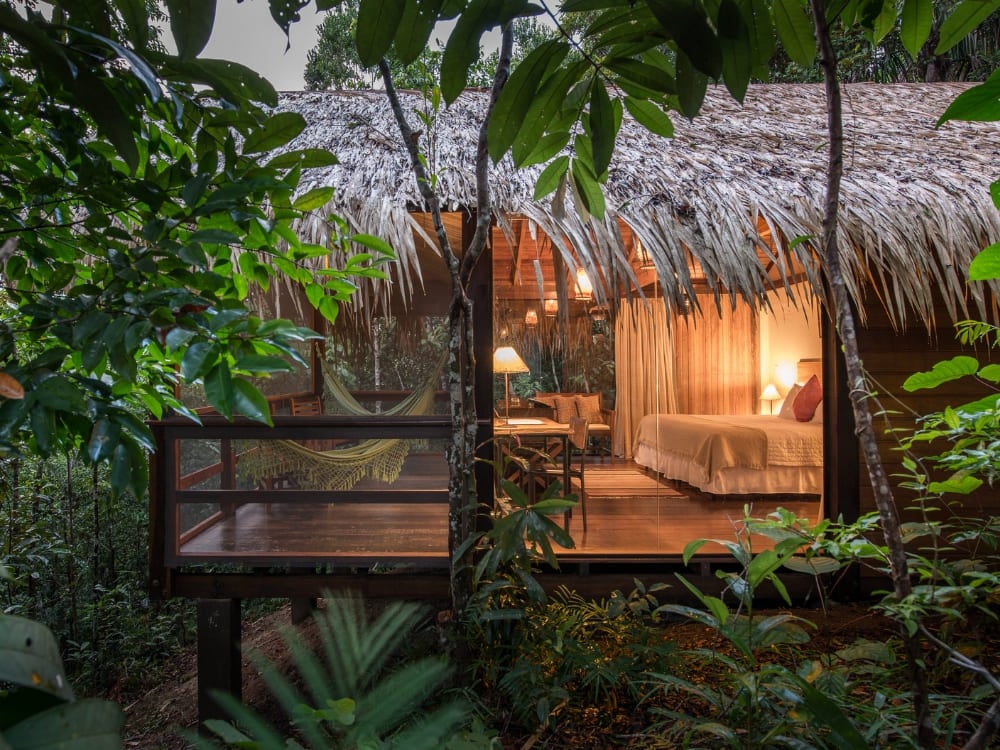 A refined bungalow with a thatched roof and a hammock on the balcony at Anavilhanas Jungle Lodge in Brazil. A refined bungalow with a thatched roof and a hammock on the balcony at Anavilhanas Jungle Lodge in Brazil.